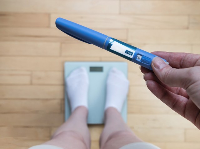 Person standing on a scale holding a semaglutide injector pen