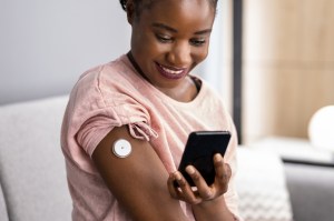Woman Testing Glucose Level With Continuous Glucose Monitor On Mobile Phone