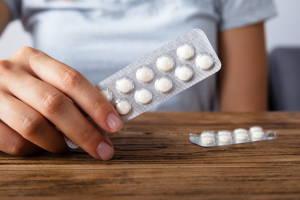 Woman's Hand Holding Medicine Over Wooden Desk