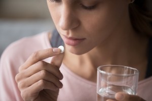 Close up cropped image millennial multiracial girl holding pill and glass of fresh water taking medicine