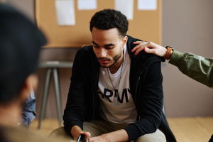 Hand of young man on shoulder of unhappy and depressed male attendant of psychological session or support group
