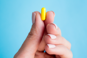 A woman's hand holding yellow pill capsule on blue background