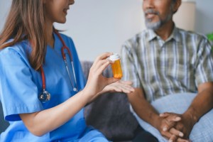 Nurse holding a pill bottle and explaining prescription to senior patient during home visit