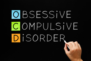 Hand writing OCD - Obsessive Compulsive Disorder with white chalk on blackboard.