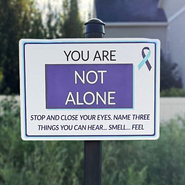 A trail sign that says, "You are not alone. Stop and close your eyes. Name three things you can hear... smell... feel"